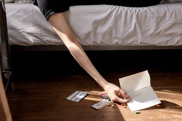 Kobieta Cropepd leży na łóżku myśląc o popełnieniu samobójstwa przez narkotyki i list — Zdjęcie stockowe