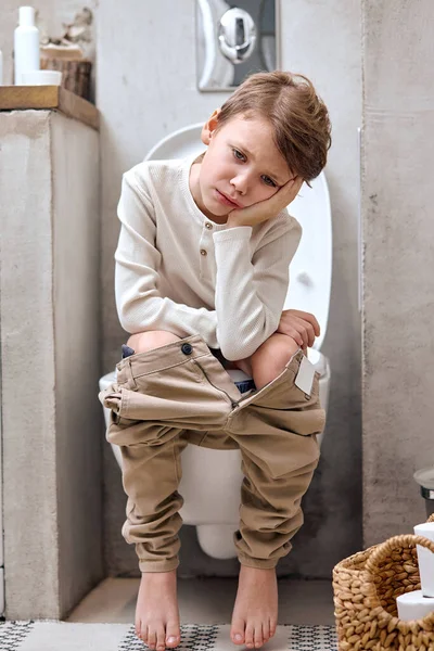 Menino da escola está sentado no banheiro com sofrimento de constipação ou hemorróidas — Fotografia de Stock