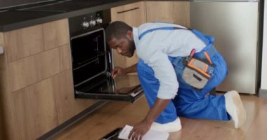 Evdeki mutfakta elektrikli fırını inceleyen siyah tamirci. Aygıt Tamiri.