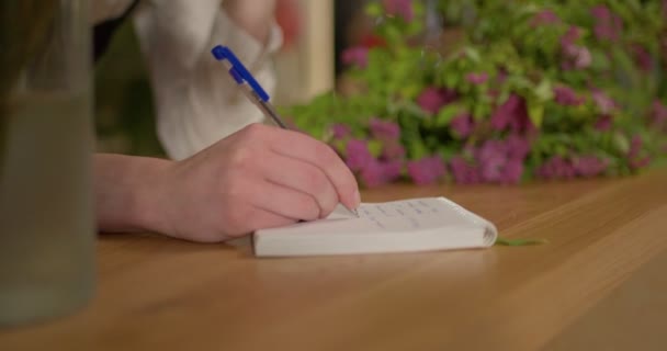 Közeli kezek virágárus nő jegyzetel a munkahelyen, írás notebook — Stock videók