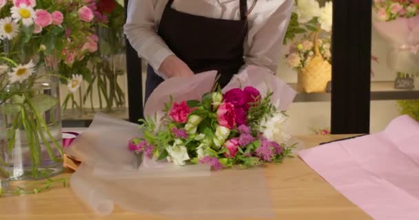 Entzückte Frau beendet die Vorbereitung eines Straußes und bedeckt Blumen mit Geschenkpapier — Stockvideo