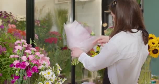 素敵な若い女性花屋は花束を飾る花の店で植物を配置します — ストック動画