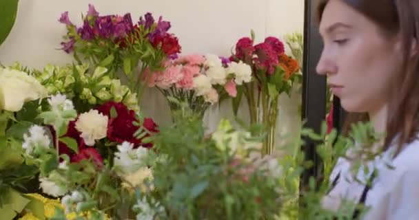 Ευχάριστο ανθοπωλείο παίρνει λουλούδια στο ψυγείο. γυναίκα με μαύρη ποδιά στολή επιλέγει λουλούδια — Αρχείο Βίντεο