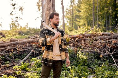 Woodman work with ax in summer forest. Strong lumberjack in plaid shirt.