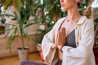 Cropped young female is practicing yoga, sitting with legs crossed on floor