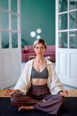 Confident Caucasian woman sitting in padmasana lotus position, at home