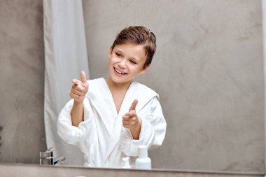 Pleasant nice child boy showing thumbs up after cleaning, shaving, smiling satisfied