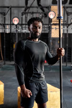 Young afro american athlete male in black sportswear holding barbell bar, preparing for training