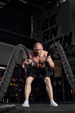 Waves of force. Young caucasian bodybuilder training with battle ropes