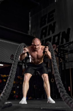 athletic young caucasian man working out with battle ropes in cross fit gym.