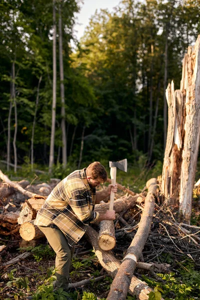 Un tizio senza barba con un'ascia taglia un tronco, tagliando alberi con un'ascia. Tecnica al lavoro. — Foto Stock