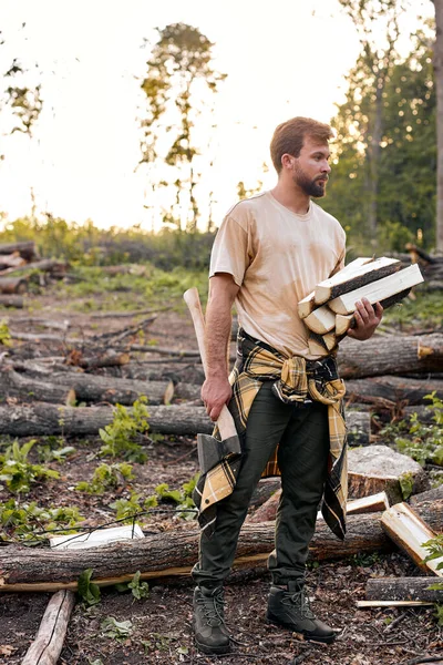 Hombre hombre trabajador leñador sosteniendo leña en las manos, al aire libre en el bosque en el día —  Fotos de Stock