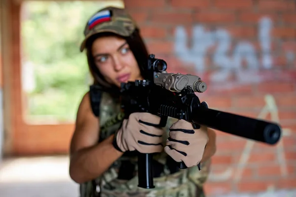 Athlete woman with rifle gun aims at target, wearing military gear, in abandoned building. — Stock Fotó