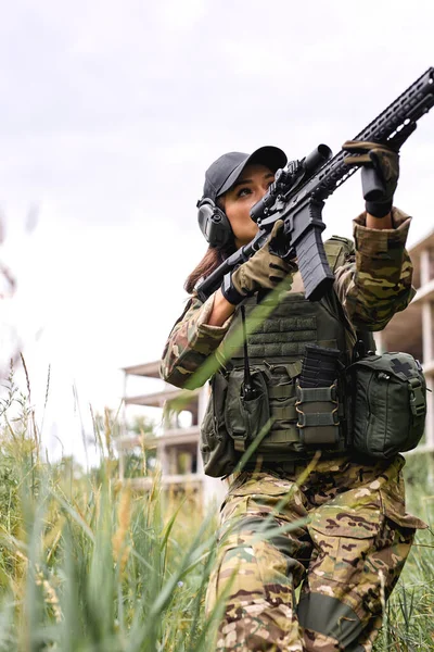 Militaire en tenue armée avec une arme à visée optique. Athlète dame dans l'herbe visant fusil — Photo