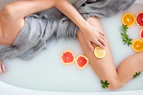 Vue de dessus sur les jambes féminines, dame est couchée dans le bain de lait avec des agrumes, photo recadrée — Photo