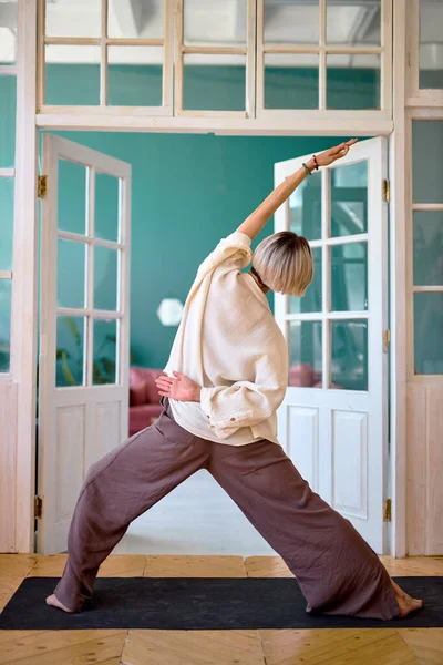 Реальный взгляд на молодую красивую фитнес-женщину делает растяжки упражнения в помещении дома — стоковое фото
