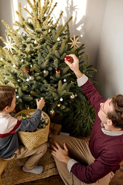 Счастливый молодой мужчина помогает маленькому ребенку украшать елку игрушками — стоковое фото