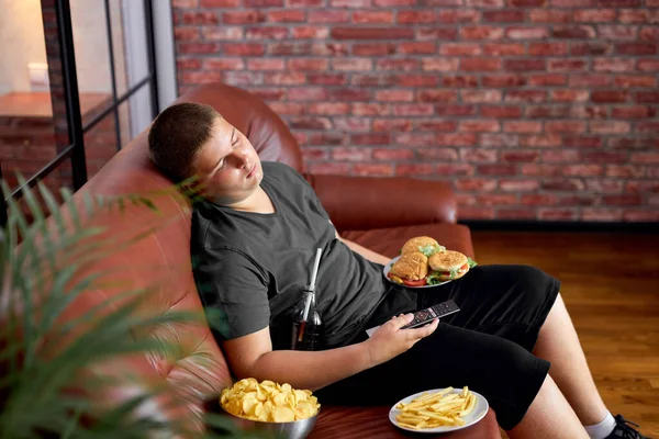 Mangiare troppo ragazzo dormire sul divano in soggiorno, giovane ragazzo adolescente caucasico addormentarsi — Foto Stock