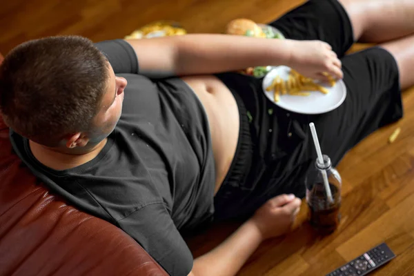 Vista dall'alto sul ragazzo obeso overweght seduto sul pavimento a mangiare patatine fritte, mangiare troppo — Foto Stock