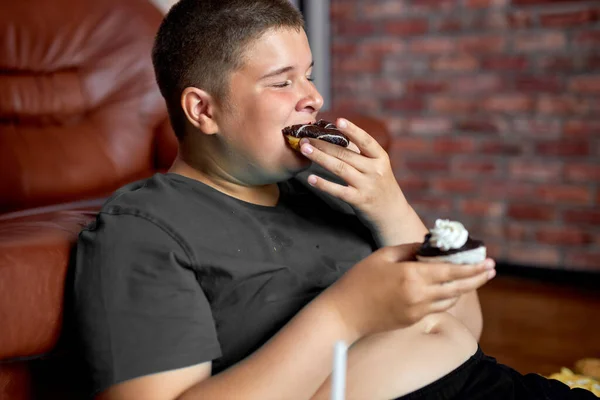 Menino adolescente comendo saborosos donuts doces em casa. Comida saborosa e não saudável — Fotografia de Stock