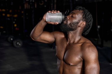 Break after hard crossfit training. Portrait of young sporty african man drinking water