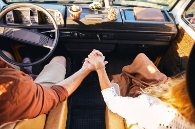 Close up of cropped couple holding hands together while driving a car.
