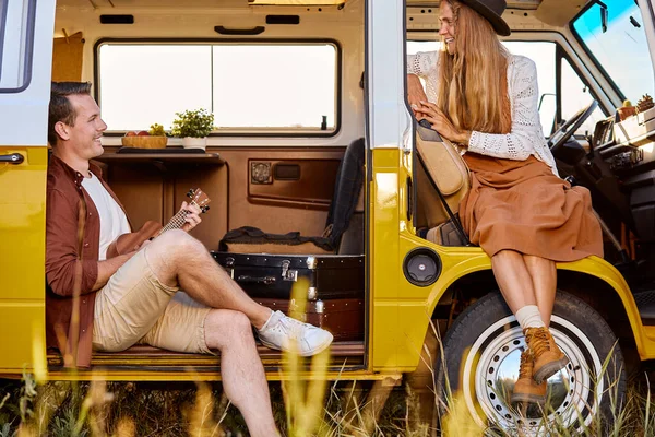 Young hipster couple playing guitar ukulele sing a song in yellow van, in nature — Stock Fotó