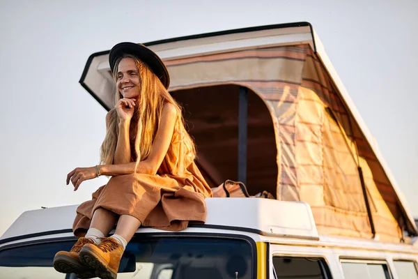Hermosa mujer tranquila con el pelo largo se sienta en el techo de la camioneta amarilla para el viaje, disfrutar —  Fotos de Stock