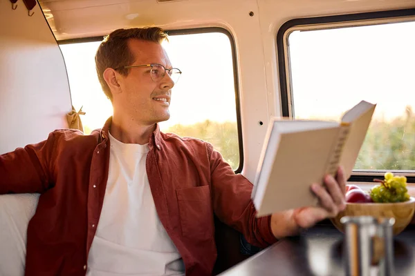 Zadowolony miły facet w okularach czyta książkę podczas podróży minivanem — Zdjęcie stockowe
