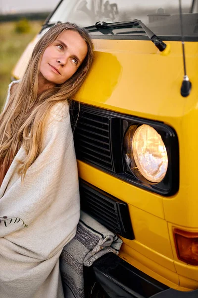 Dream woman is looking at side, posing, sitting on ground next to yellow van — стоковое фото