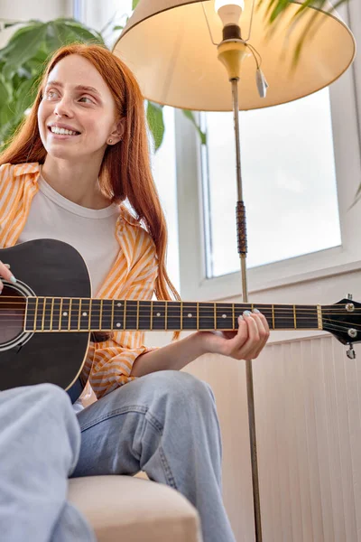 Dame ouverte d'esprit avec des cheveux roux naturels en tenue décontractée jouant de la guitare acoustique, à la maison — Photo