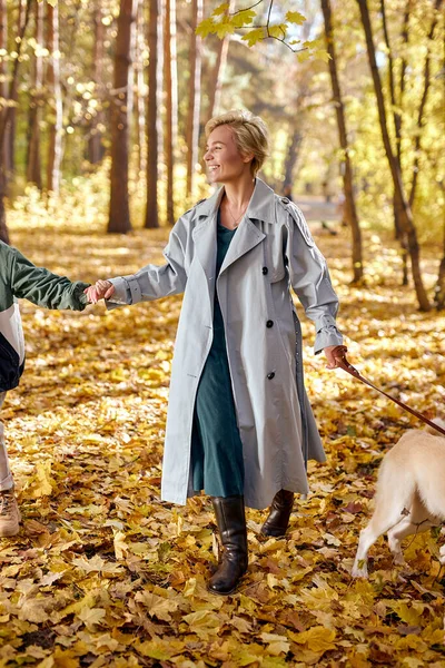 Heyecanlı, ceketli, oğluyla köpek gezdiren, eğlenen bir kadın. — Stok fotoğraf