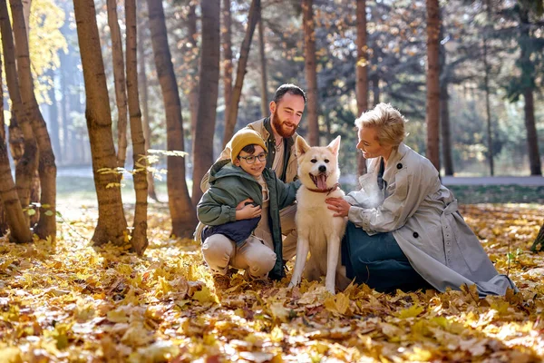 Jovem família caucasiana com cão de estimação relaxar enquanto caminha no parque, na temporada de outono — Fotografia de Stock