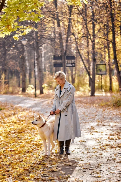 Mulher atraente andando, se divertindo com o cão ao ar livre. senhora loira de casaco — Fotografia de Stock
