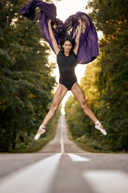 Genç, güzel esmer balerin ormanda yol kenarında sicimle atlıyor.