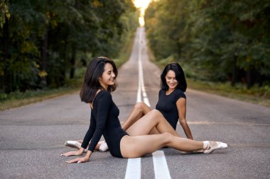 İki gülümseyen romantik balerin kadın gün batımında yolda dinleniyor ve oturuyor.