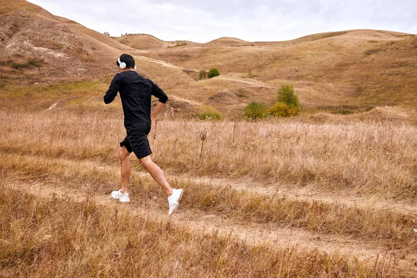 Konzentrierter Mann im schwarzen Trainingsanzug läuft morgens auf dem Feld, treibt Sport — Stockfoto