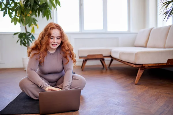 Online kişisel antrenörden ders almak için dizüstü bilgisayar kullanan kızıl saçlı şişman kadın. — Stok fotoğraf