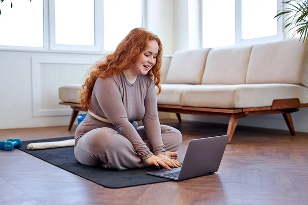 Evde dizüstü bilgisayar kullanarak çevrimiçi fitness kursuna hazırlanan tombul bir kadın. — Stok fotoğraf