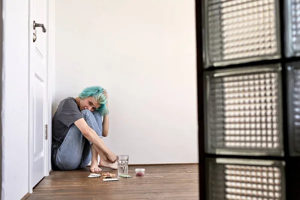 Chateado jovem mulher sentada no chão e chorando, com pílulas, pensando em suicídio — Fotografia de Stock