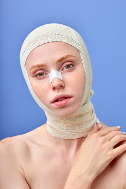 Mavi stüdyo arka planında ameliyattan sonra tıbbi bandajlı kadın yüzü. Boşluğu kopyala