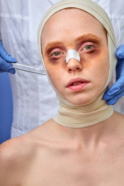 Burnu alçılı ve başı bandajlı mutsuz bir kadının portresi.