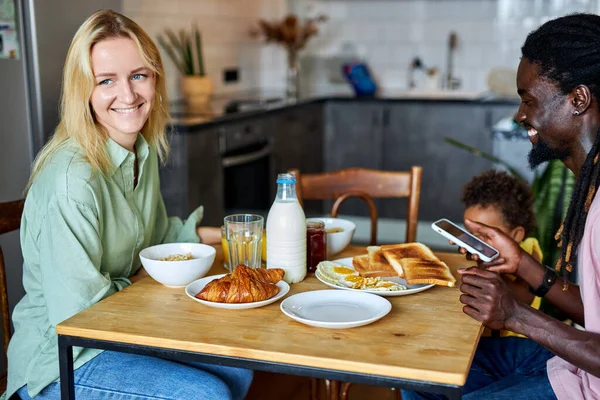 Family having meal and using smartphone, parents with child in cozy kitchen — Φωτογραφία Αρχείου