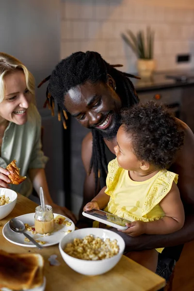 Οικογένεια έχοντας το γεύμα και τη χρήση smartphone, γονείς με παιδί στη ζεστή κουζίνα — Φωτογραφία Αρχείου