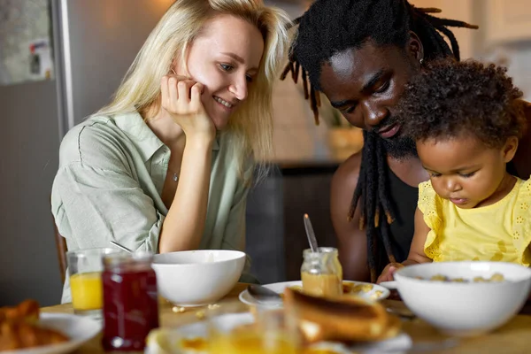 Різноманітна мати, батько снідав з дочкою, сидячи за столом з їжею — стокове фото