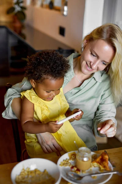 Aranyos gyermek lány néz video rajzfilmek okostelefon, miközben étkezés anyával — Stock Fotó
