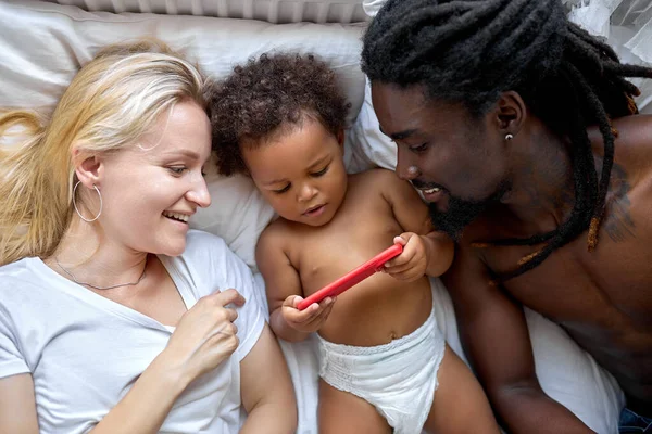 Feliz familia con hija divertirse ocio con gadget samrtphone acostado en la cama — Foto de Stock