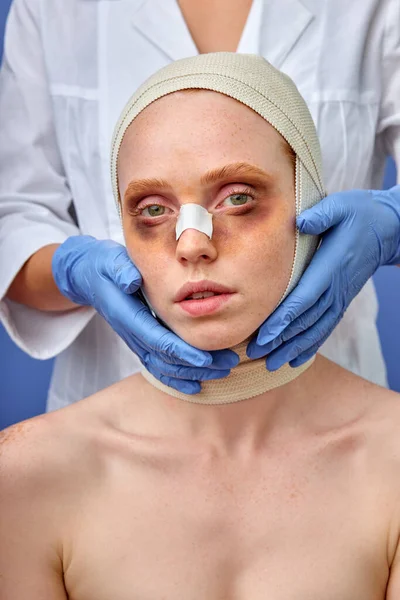 Hona med bandage över huvudet, läkare vidrör efter operation. isolerad blå bakgrund, studio skott — Stockfoto