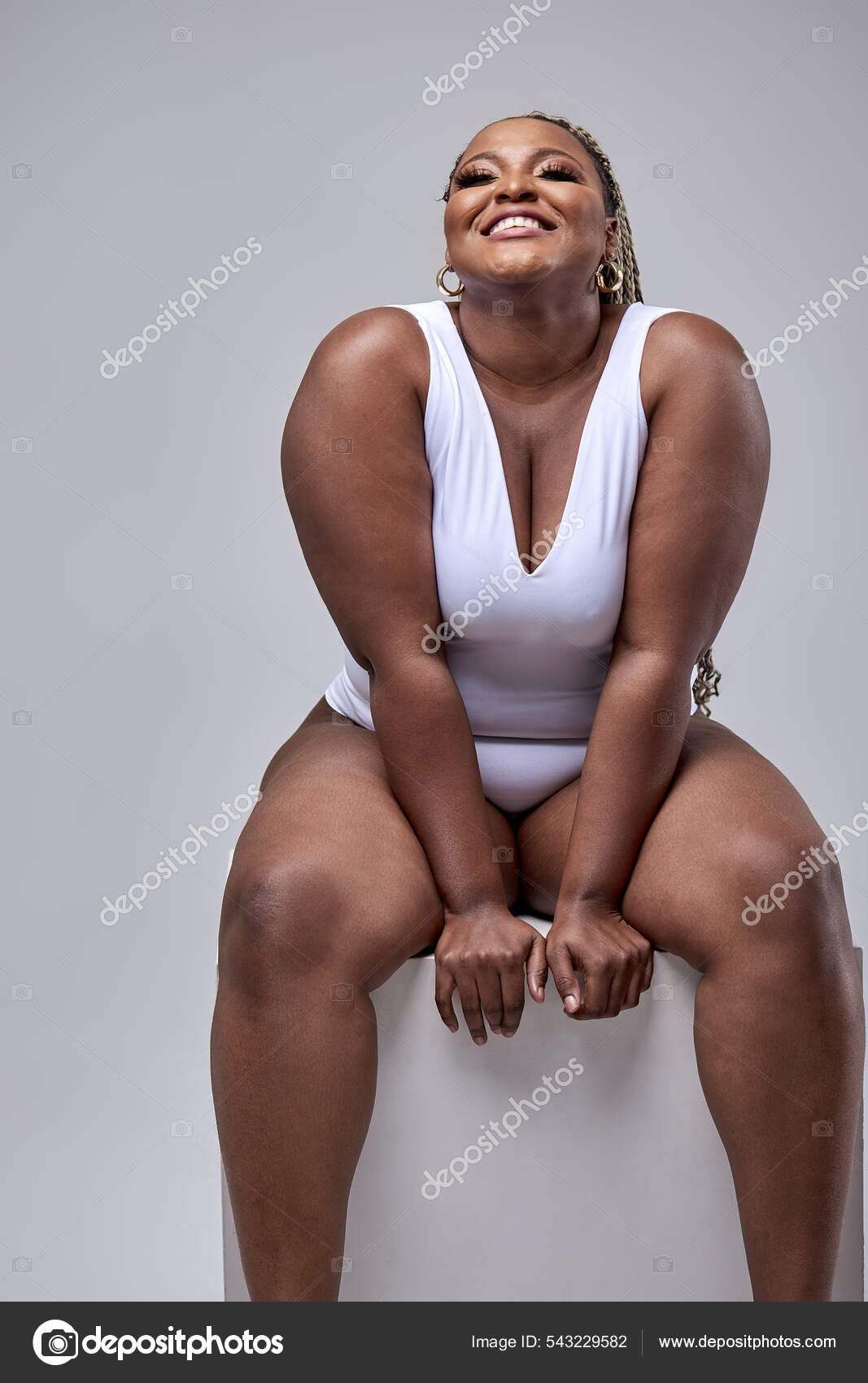Cheerful fat black woman in white bodysuit on white background