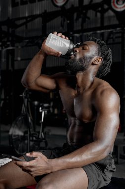 Spor eğitiminden sonra içme suyu içen genç siyahi erkek portresi.